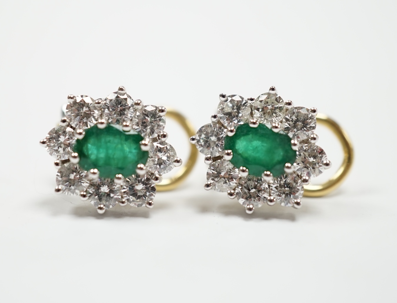 A modern pair of 18ct gold, emerald and diamond set oval cluster earrings, 13mm, gross weight 5.3 grams.